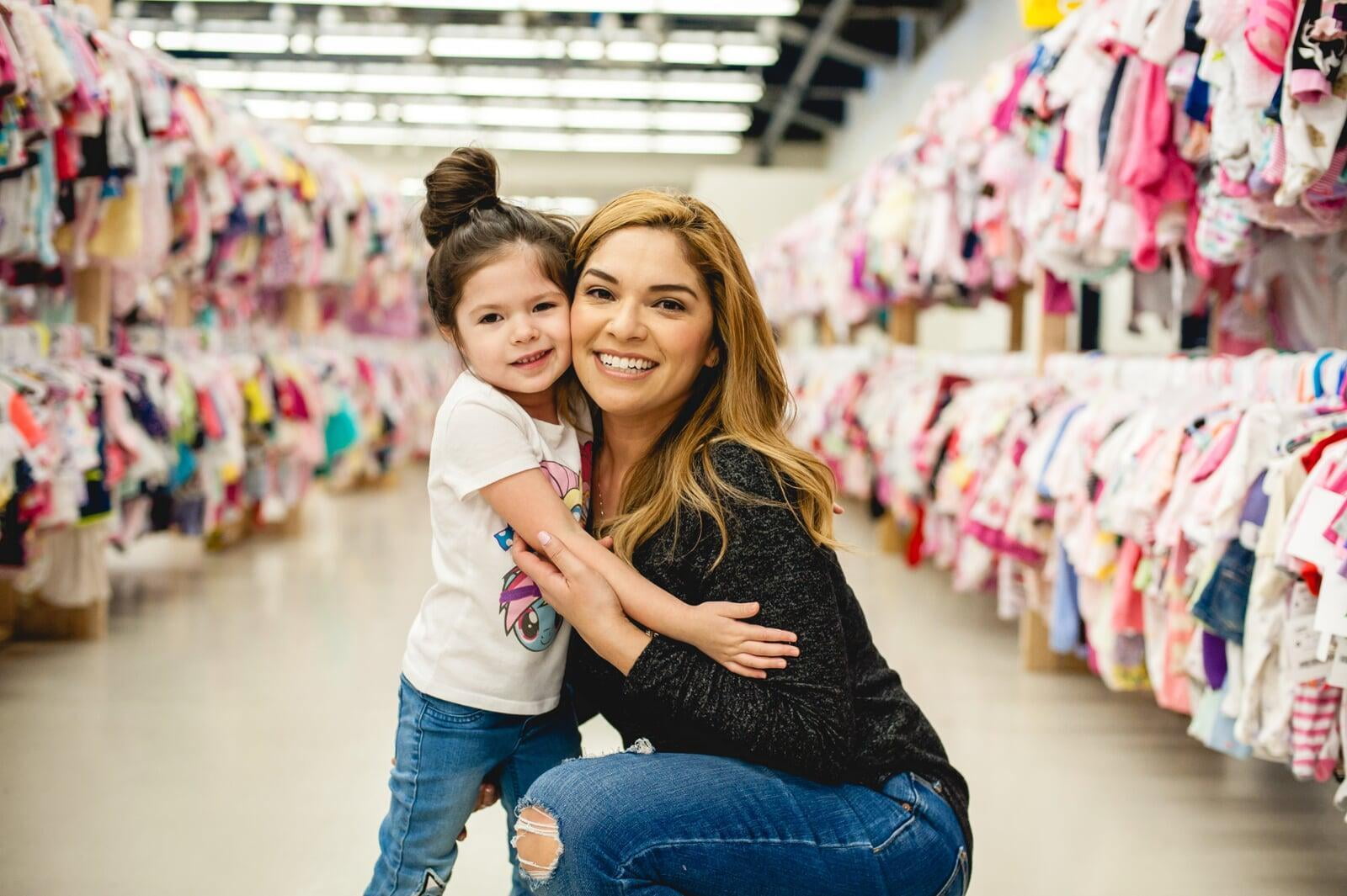 A mom and her child hug in between two rows of little girl clothes